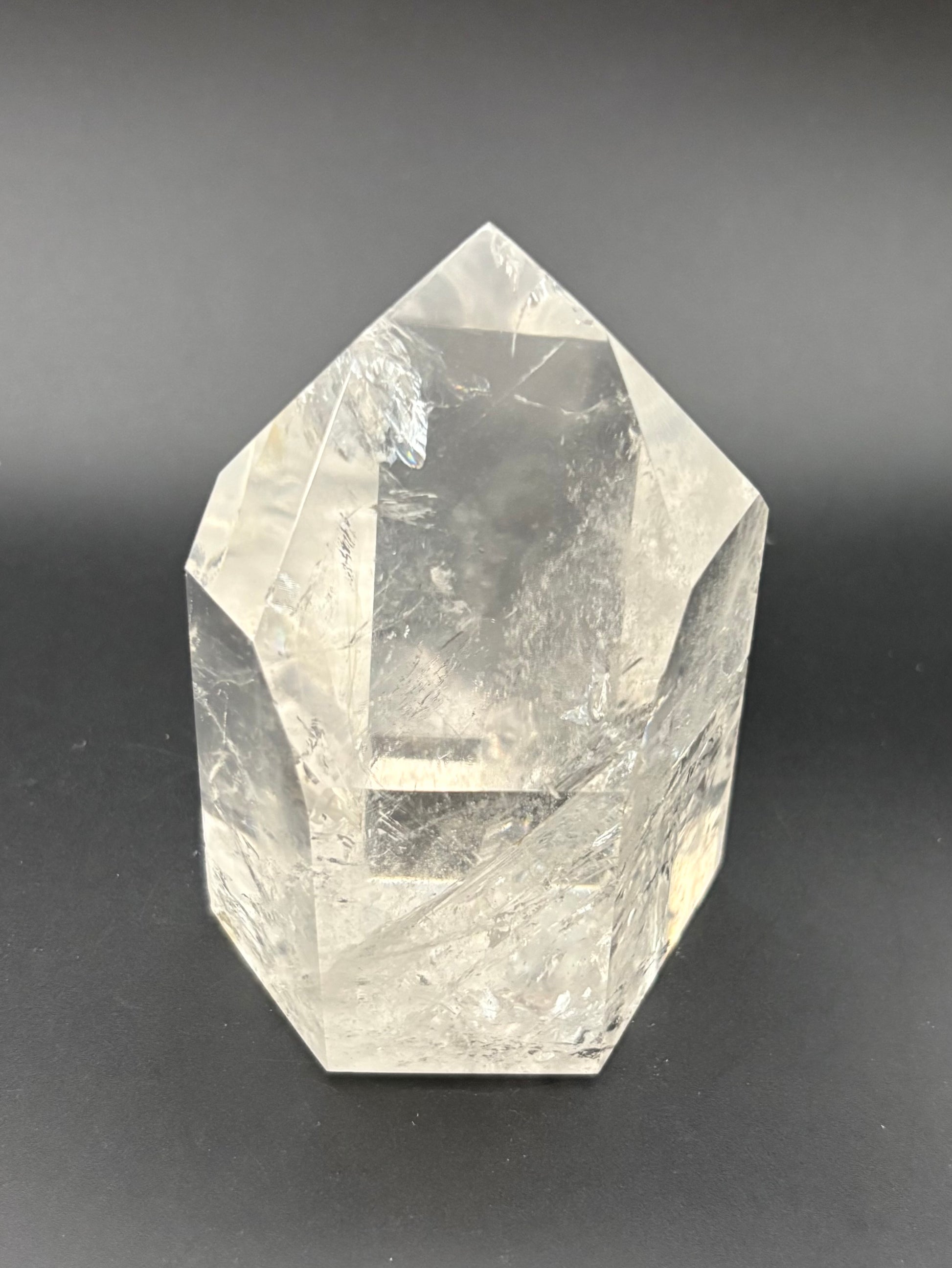 A clear faceted quartz crystal point, with natural internal inclusions, photographed on a dark gray background.