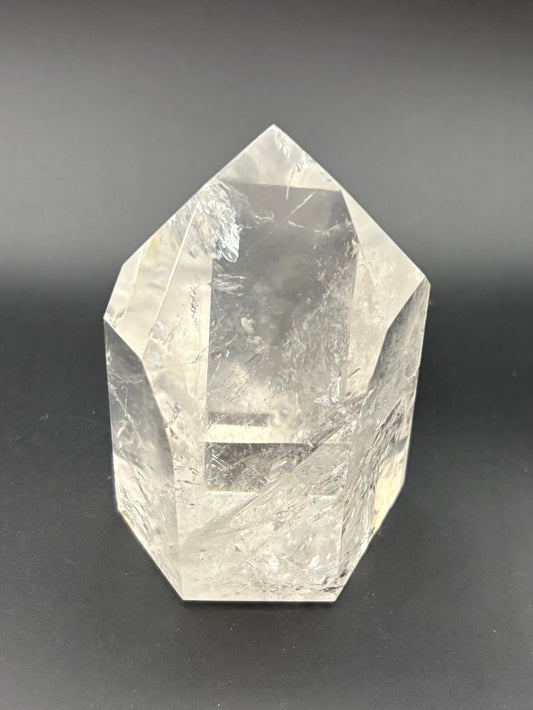 A clear faceted quartz crystal point, with natural internal inclusions, photographed on a dark gray background.