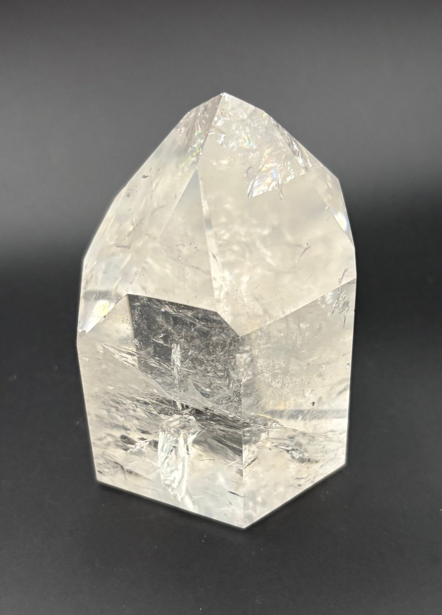 A clear faceted quartz crystal point, with natural internal inclusions, photographed on a dark gray background.