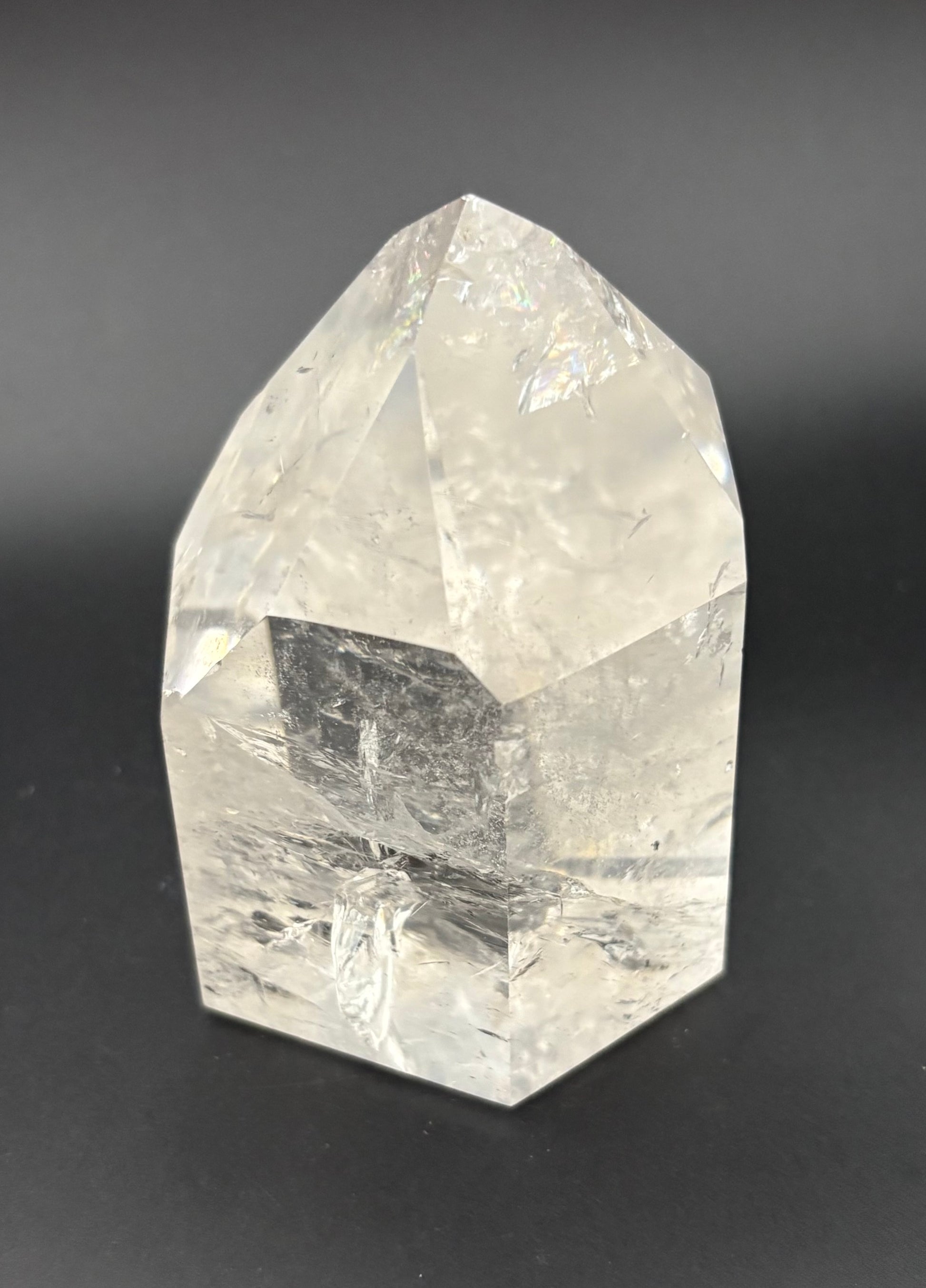 A clear faceted quartz crystal point, with natural internal inclusions, photographed on a dark gray background.