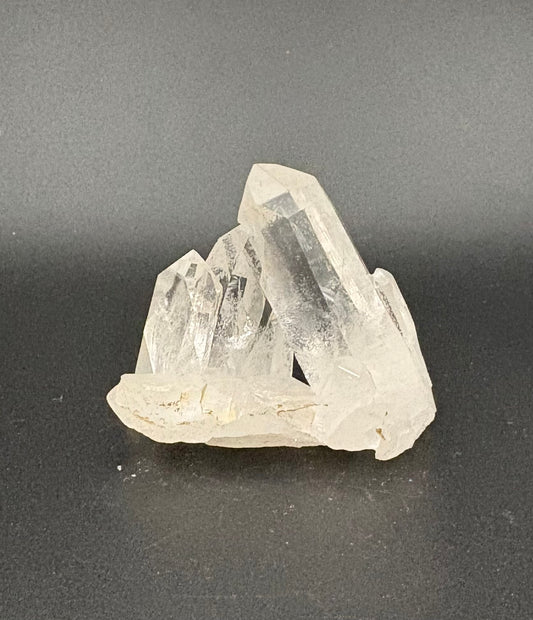 A cluster of natural clear quartz crystal points resting on a dark gray surface.