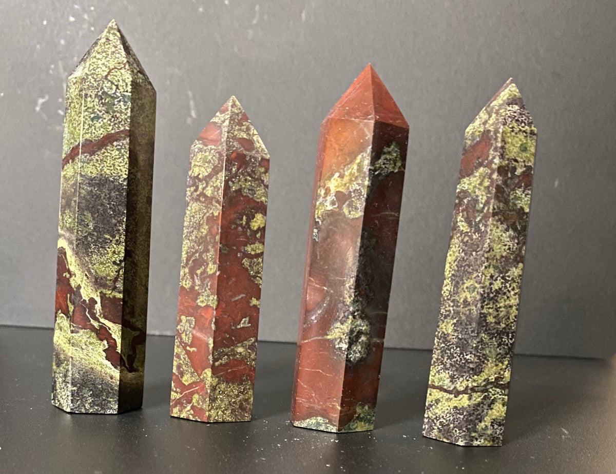 Four polished crystal point Dragon's Blood Jasper towers of varying heights and patterns, displayed on a dark surface against a gray background.