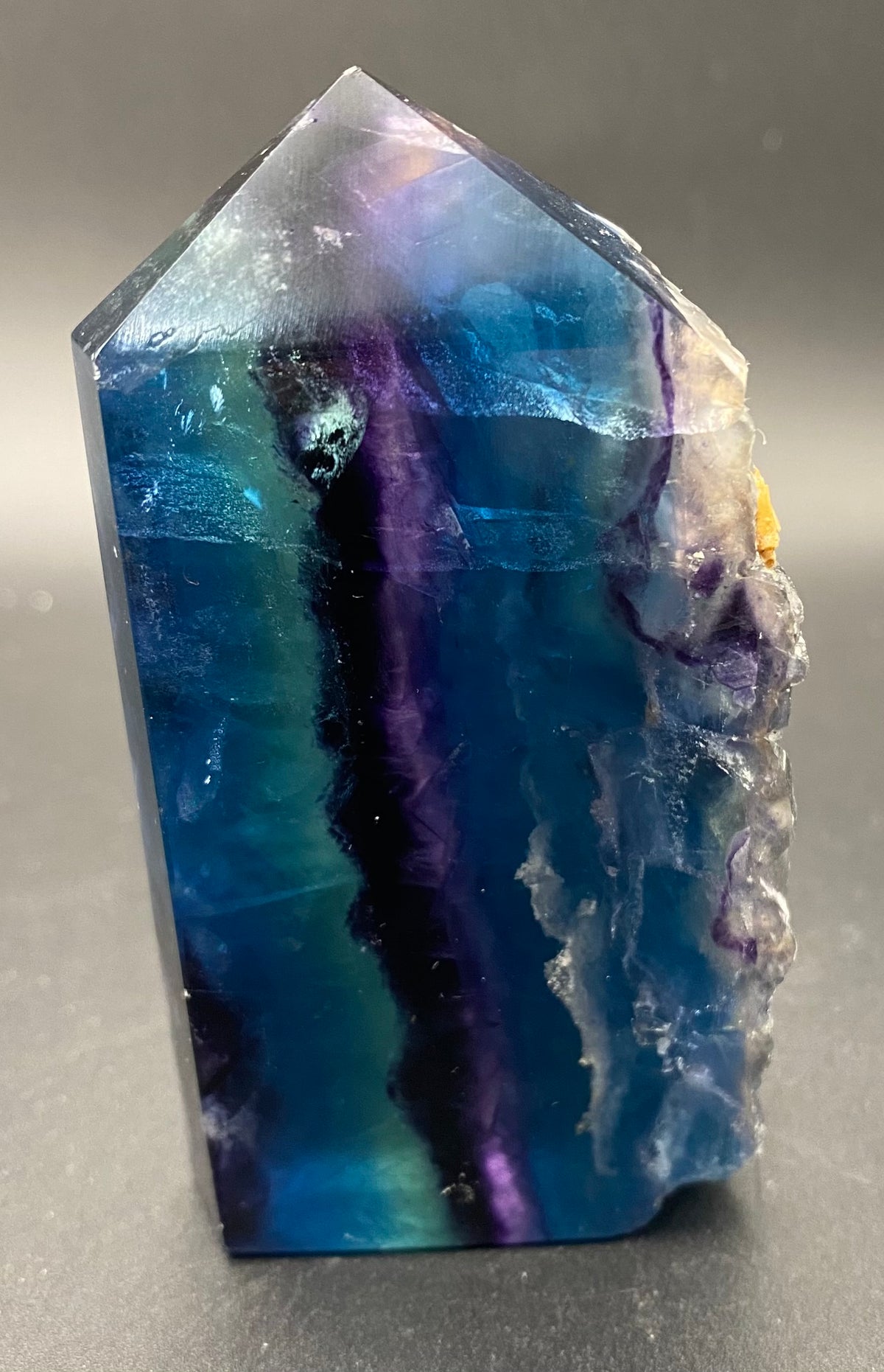 A fluorite pointed crystal tower or geode specimen with vibrant blue, purple, and teal bands, photographed on a dark gray background.