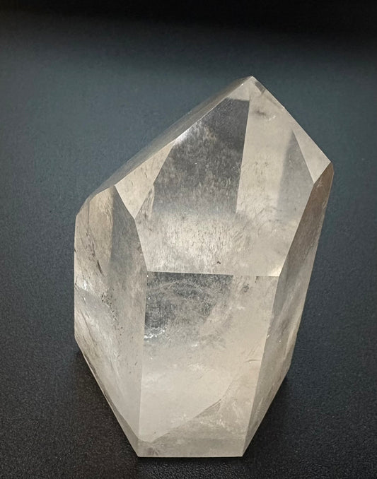 A faceted clear quartz crystal point resting on a dark, textured surface.