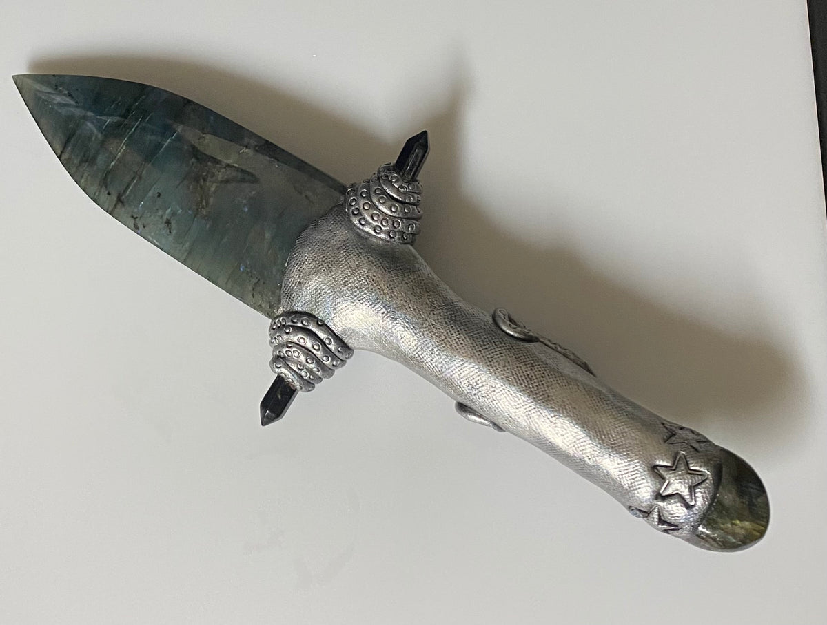 A decorative dagger with a textured silver-toned metal handle and a dark, polished stone labradorite blade, resting diagonally on a plain light background.