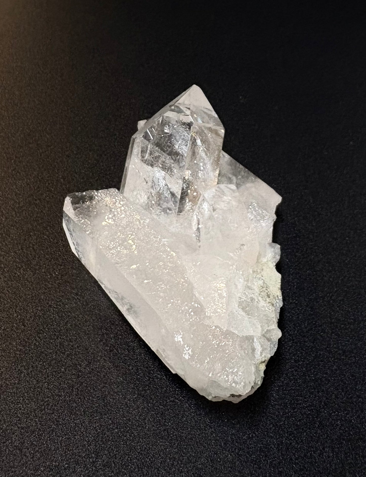A raw, unpolished clear quartz crystal cluster with prominent points and natural impurities, displayed on a dark textured background.