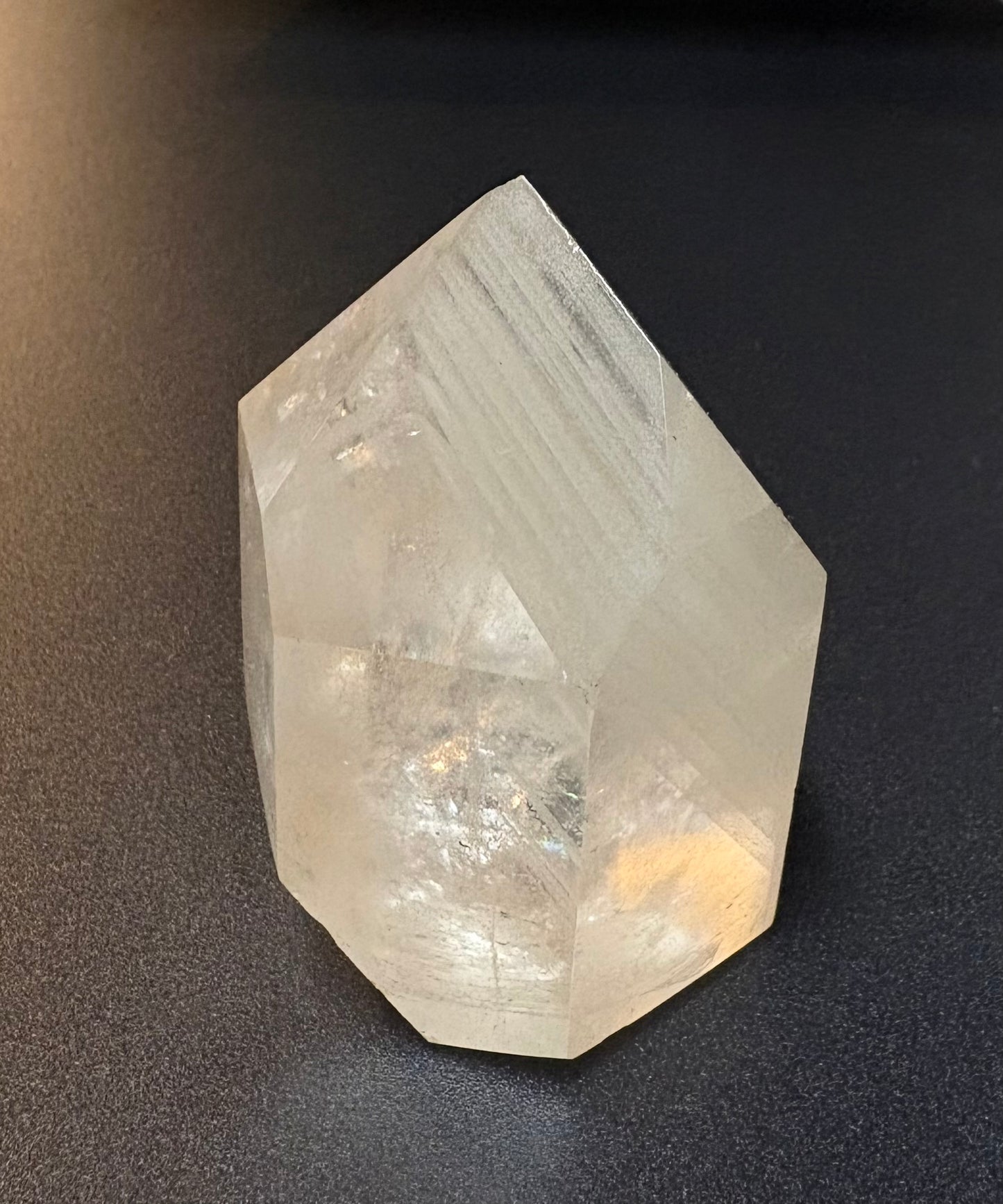 A natural clear quartz crystal point with visible internal striations, photographed on a dark textured surface.