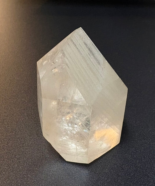 A natural clear quartz crystal point with visible internal striations, photographed on a dark textured surface.