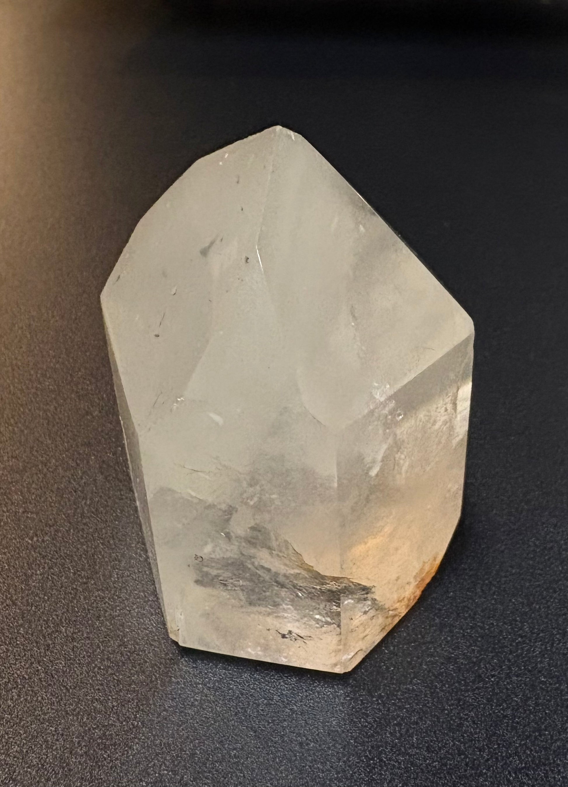 A raw, unpolished translucent crystal with natural facets, resting on a dark textured surface.