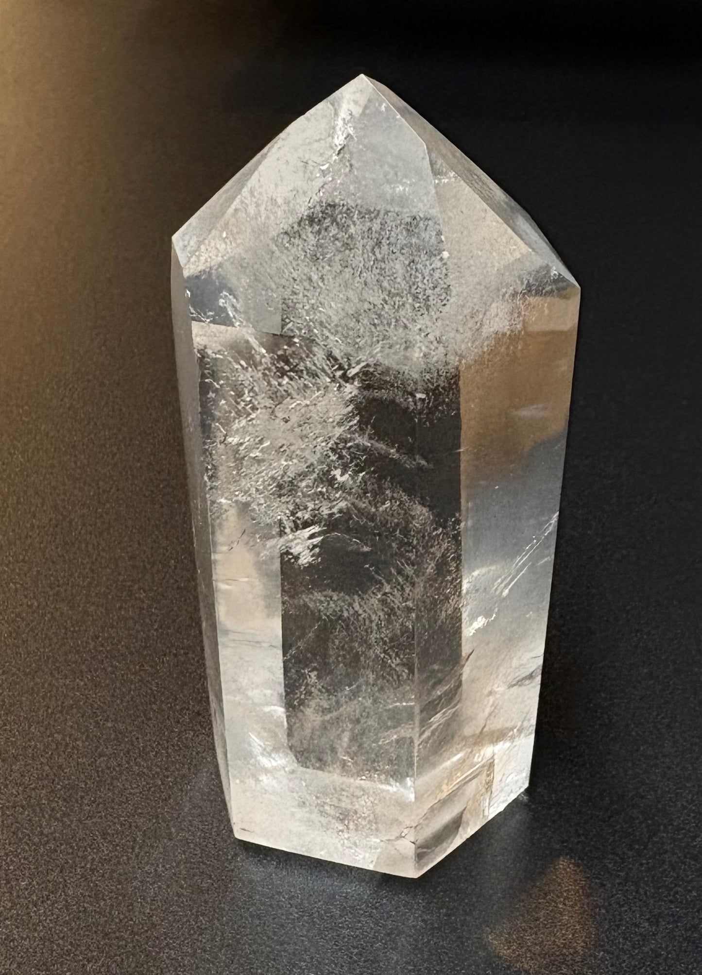 A clear quartz crystal point tower with natural inclusions and cloudy internal structures, standing on a dark surface.