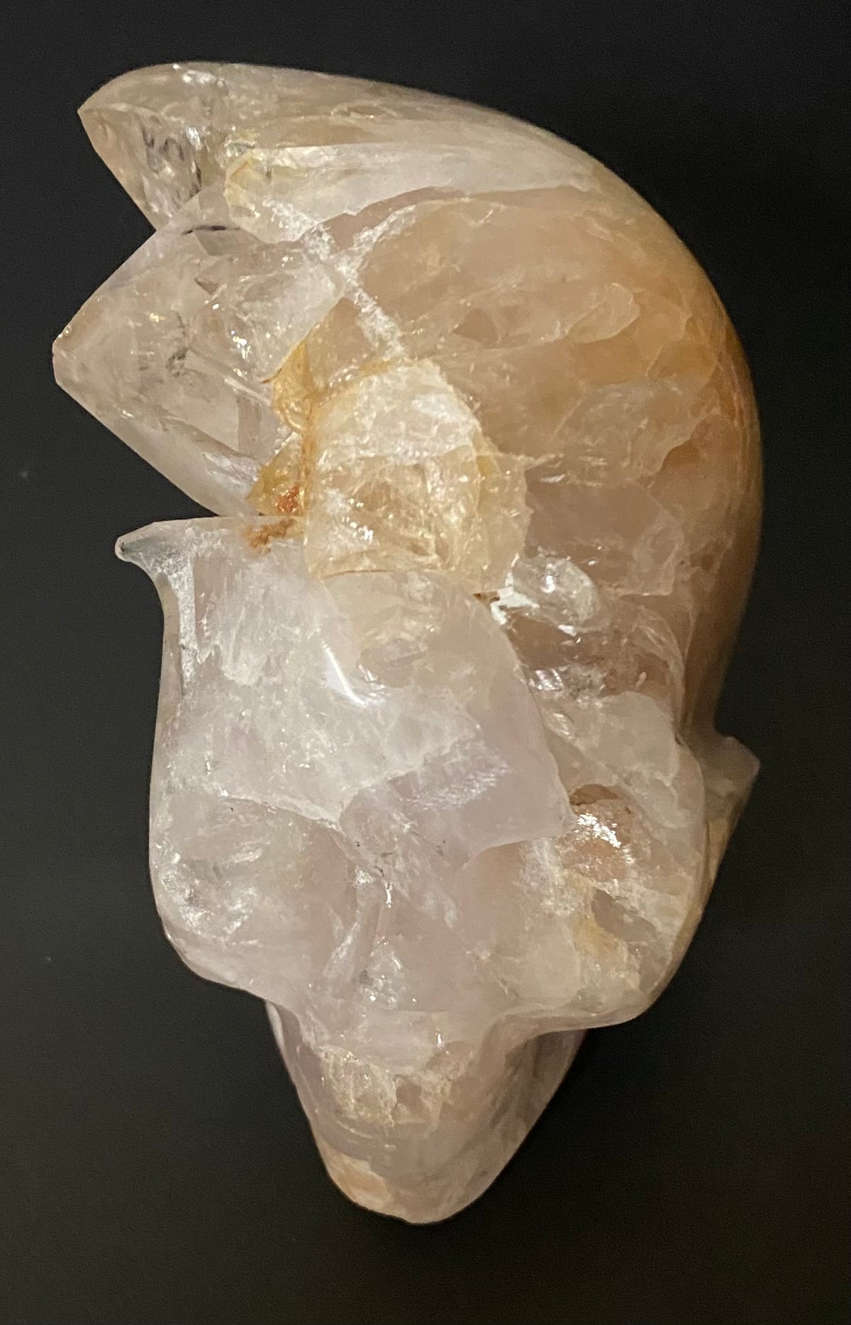 A carved crystal skull sculpture made from super seven quartz, set against a solid black background.