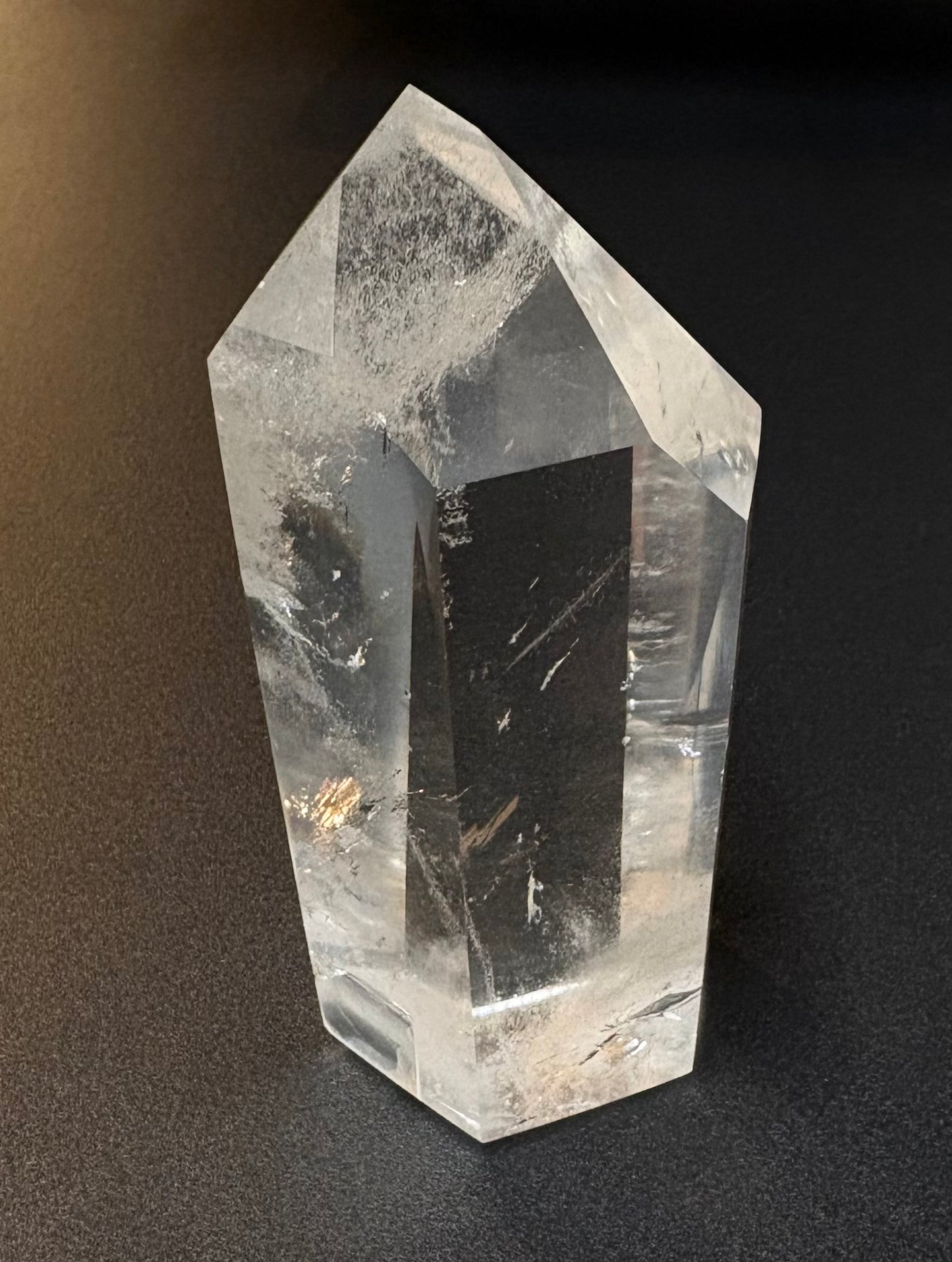 A clear quartz crystal point tower with natural inclusions and striations, photographed on a dark textured background.