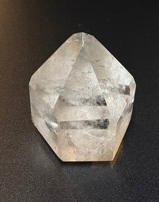 A faceted clear quartz crystal point with natural inclusions, photographed on a dark textured surface.