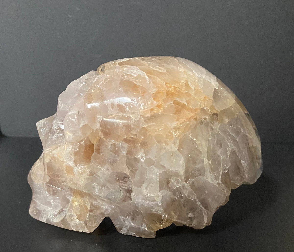A raw, rough crystal mineral specimen with a rounded organic shape, featuring translucent super seven, set against a dark gray background.