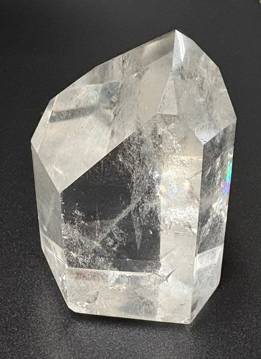 A natural clear quartz crystal point with internal inclusions, photographed on a dark textured background.