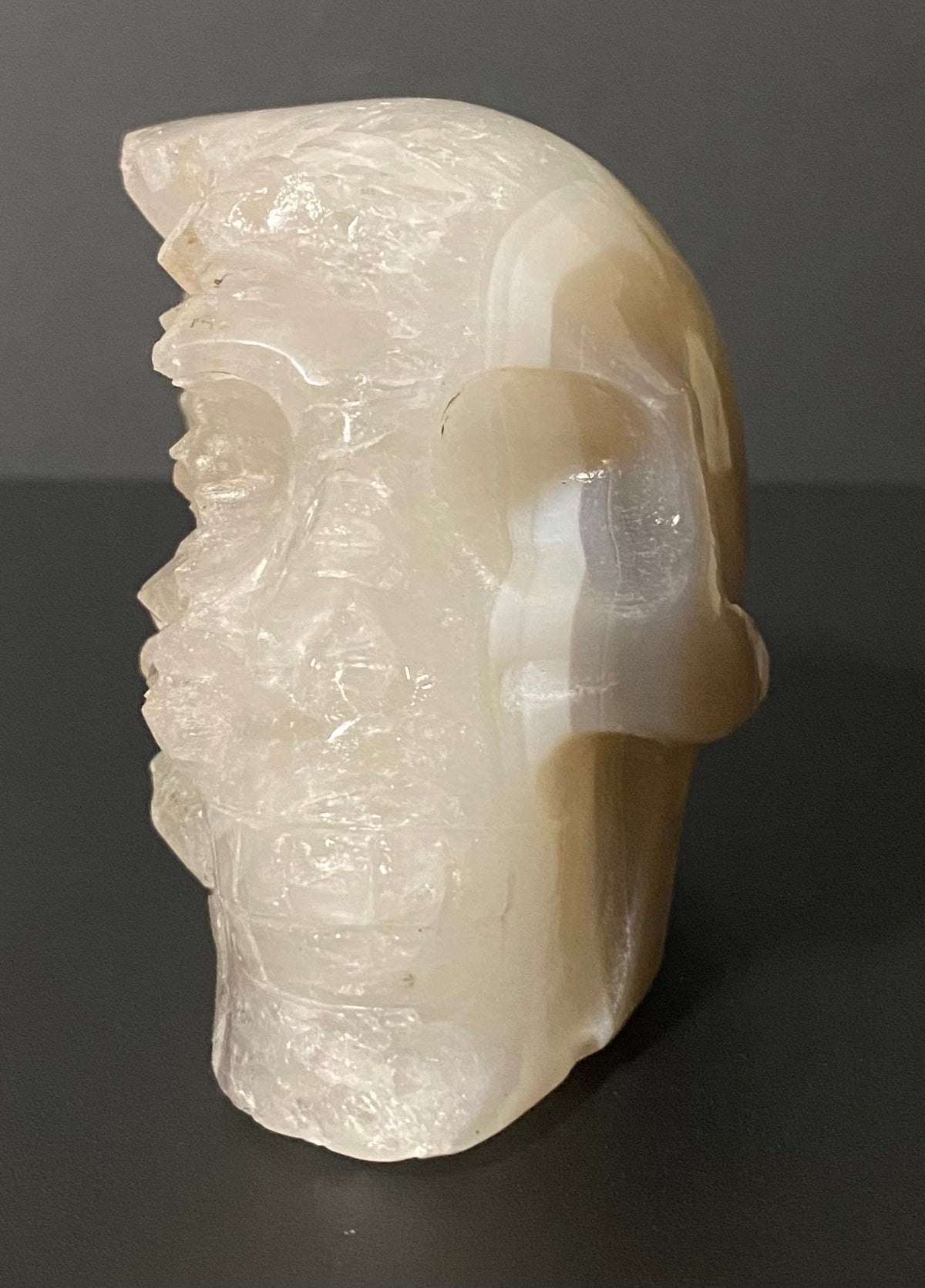 A carved skull sculpture made from milky translucent Botswana agate and quartz, set against a dark gray background.