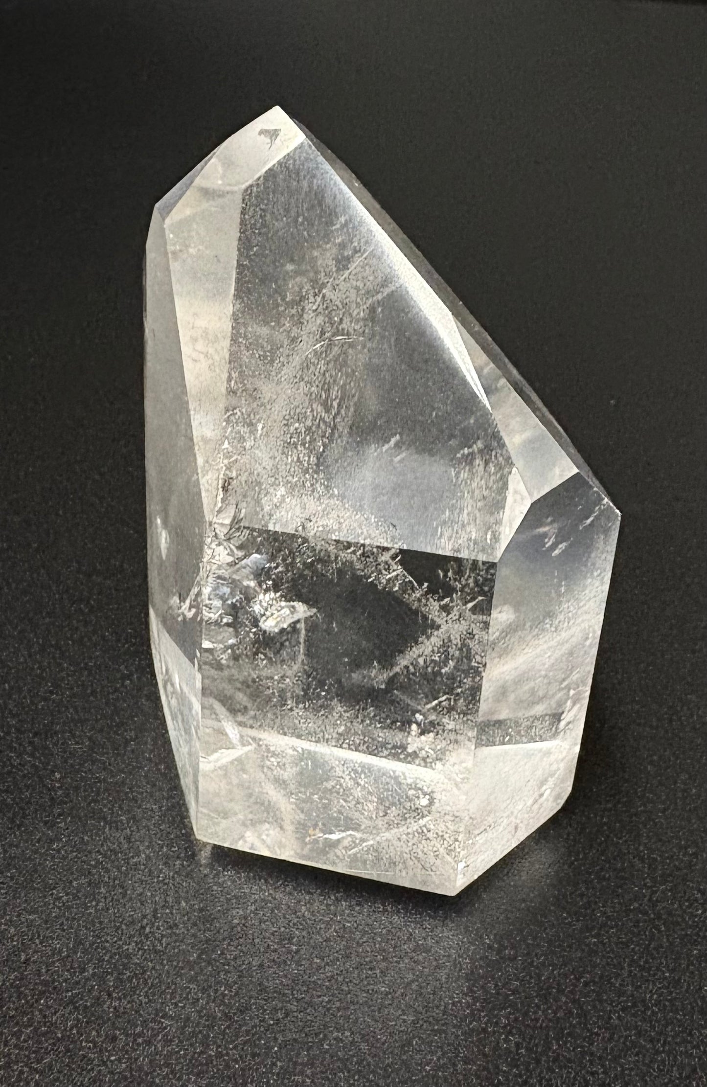 A clear quartz crystal point with visible internal inclusions, photographed on a dark textured background.