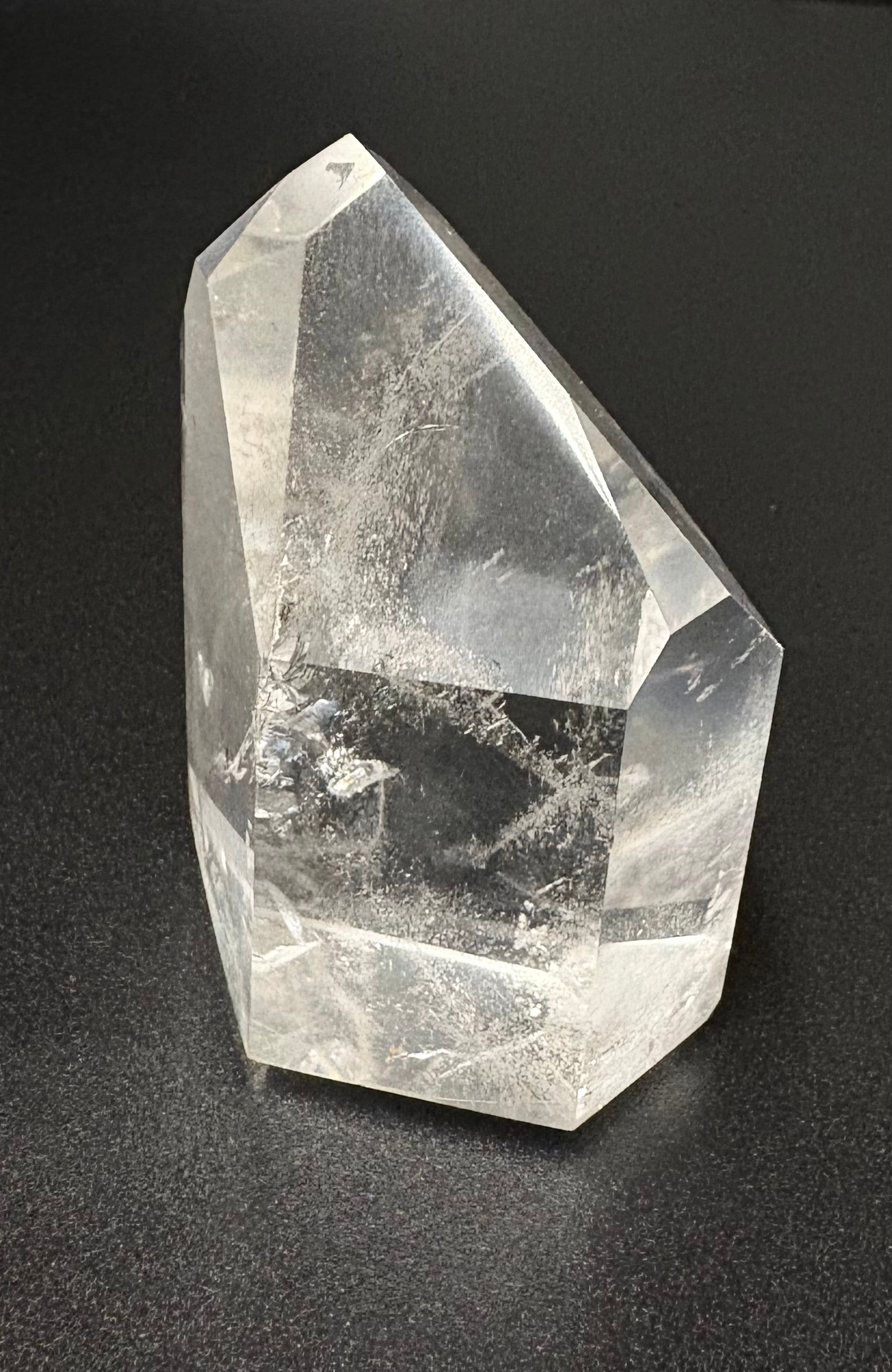 A clear quartz crystal point with visible internal inclusions, photographed on a dark textured background.