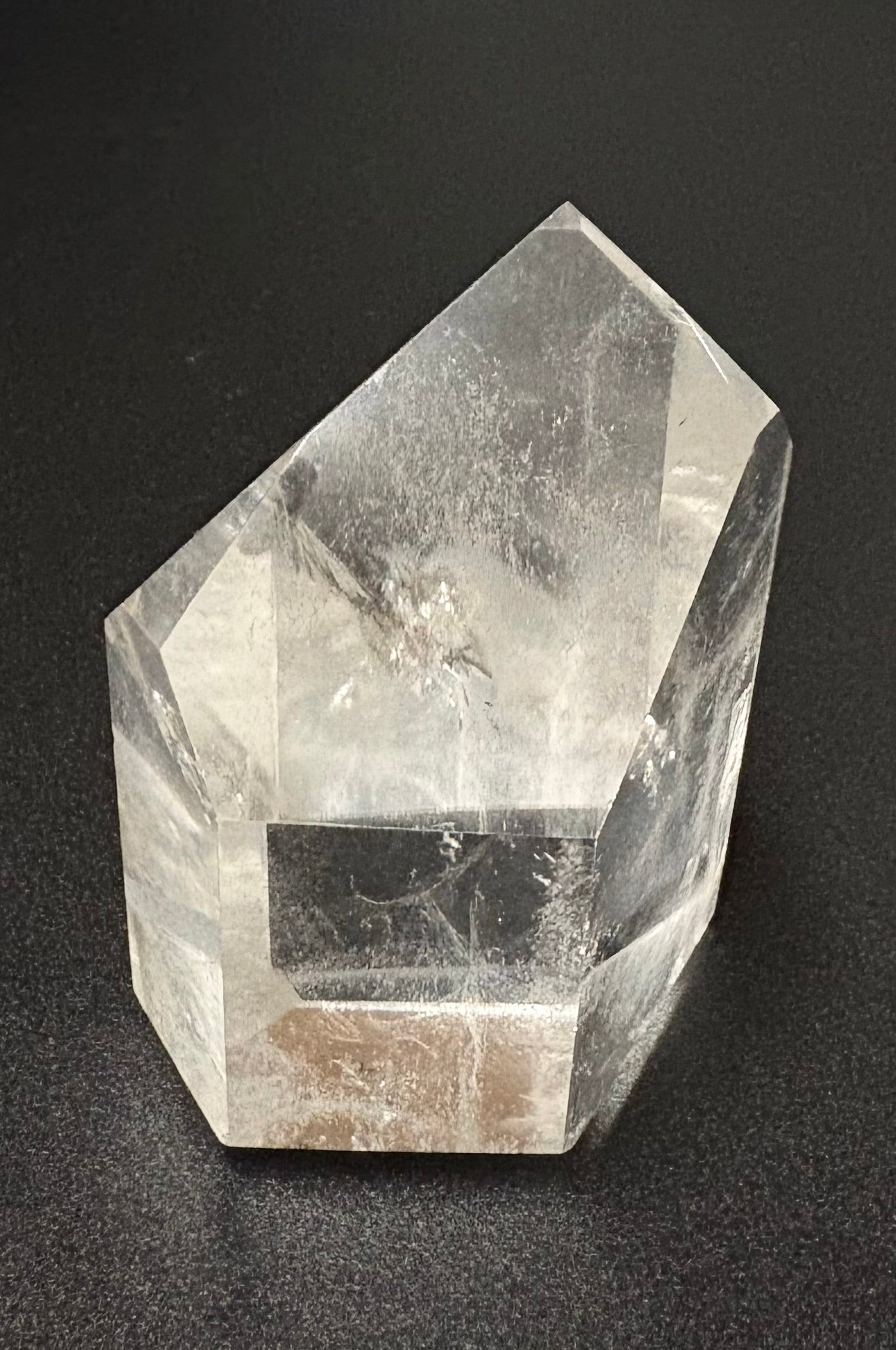A clear quartz crystal point sculpture with natural inclusions, photographed on a dark textured background.
