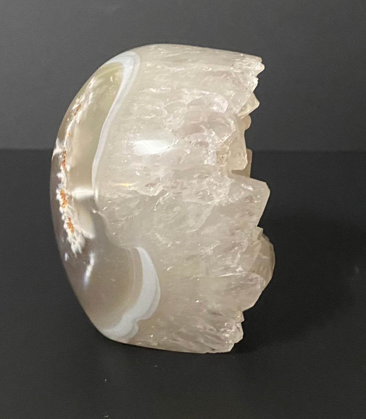 A polished raw Botswana agate and quartz stone sculpture with organic, looking curves and rough crystalline edges, displayed on a dark background.