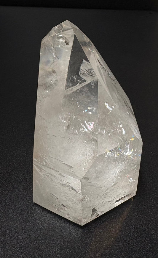 A clear quartz crystal point with natural inclusions, displayed on a dark textured background.