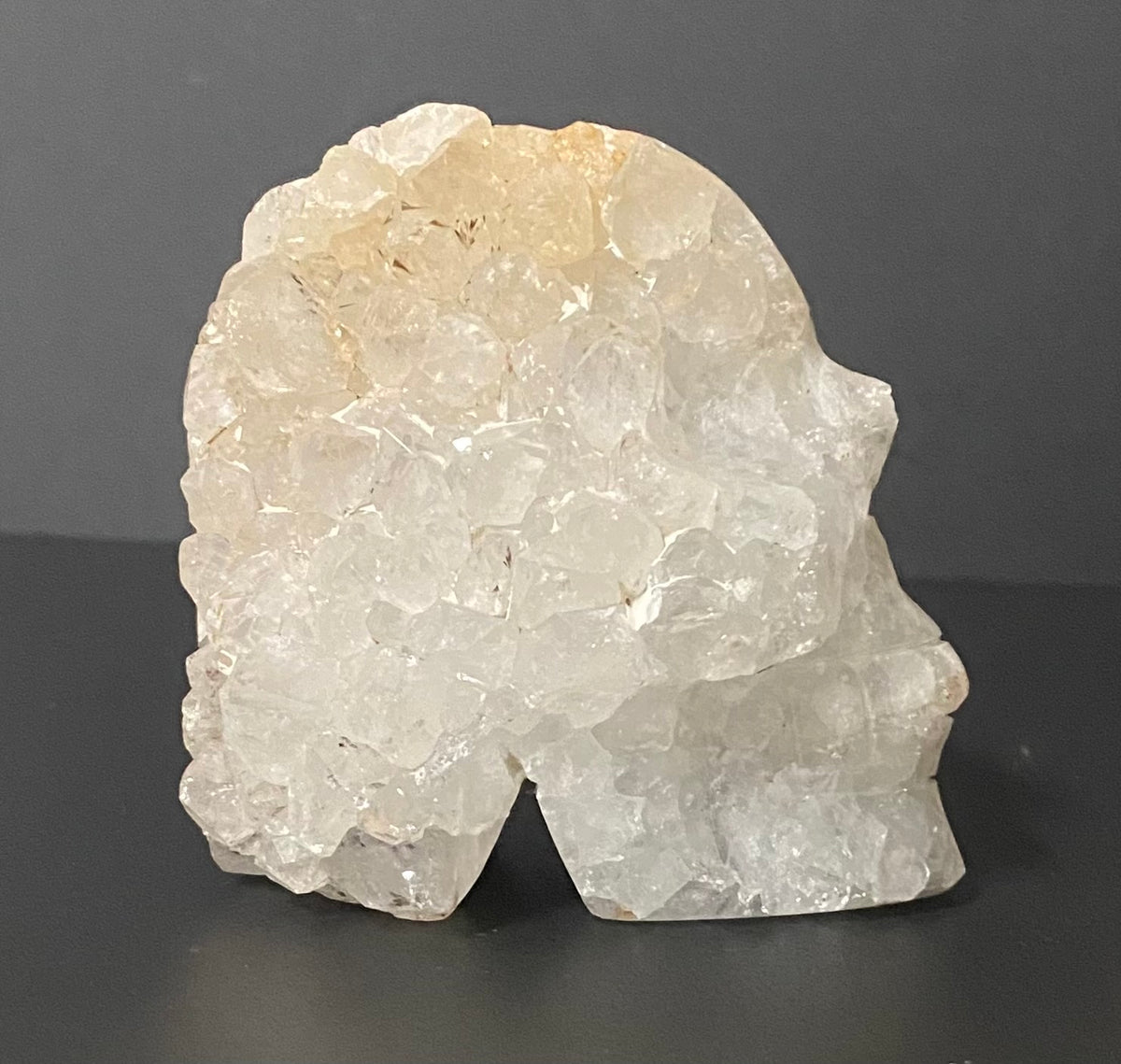 A raw, rough Botswana agate and quartz crystal head sculpture, standing on a dark gray surface against a dark gray background.