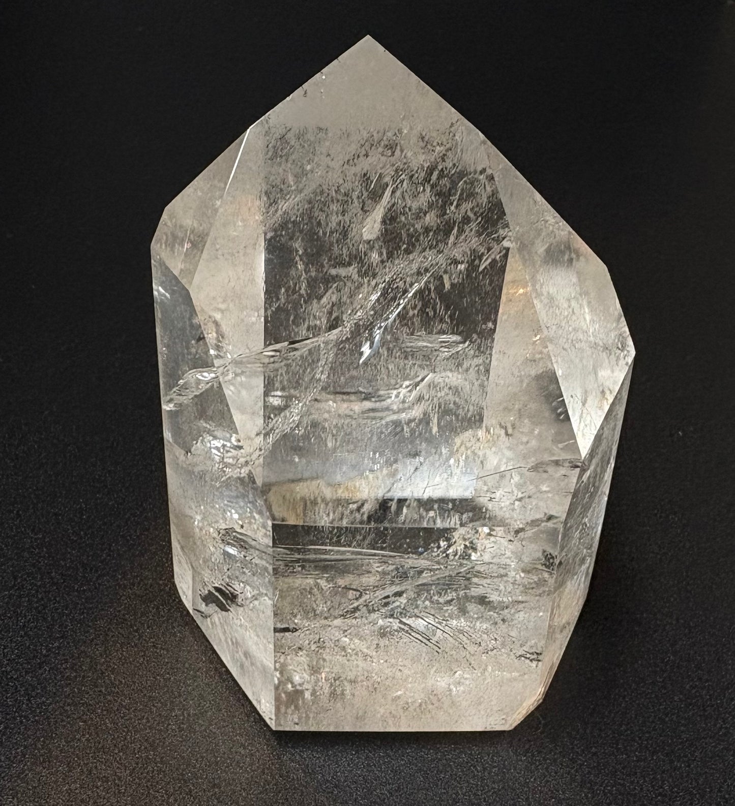 A clear quartz crystal point with visible internal inclusions and striations, photographed against a dark black background.