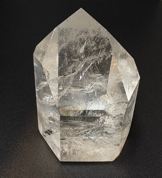 A clear quartz crystal point with visible internal inclusions and striations, photographed against a dark black background.