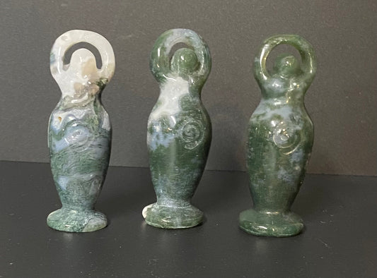 Three small green stone Moss Agate figurines with white marbled patterns, standing on a dark surface against a dark gray background.