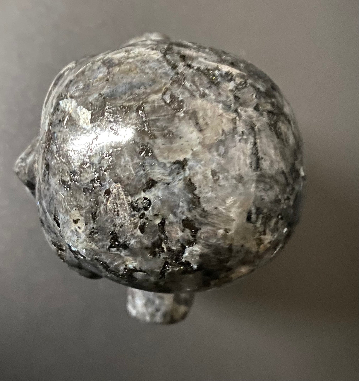 A polished gray stone Larvikite sculpture of a stylized head, photographed from a top-down angle against a neutral gray background.