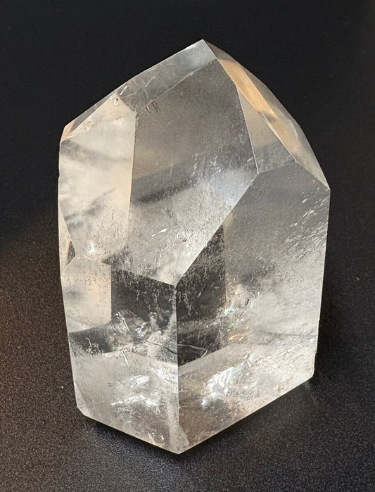A natural clear quartz crystal point with visible internal inclusions and faceted geometric edges, photographed against a dark black background.
