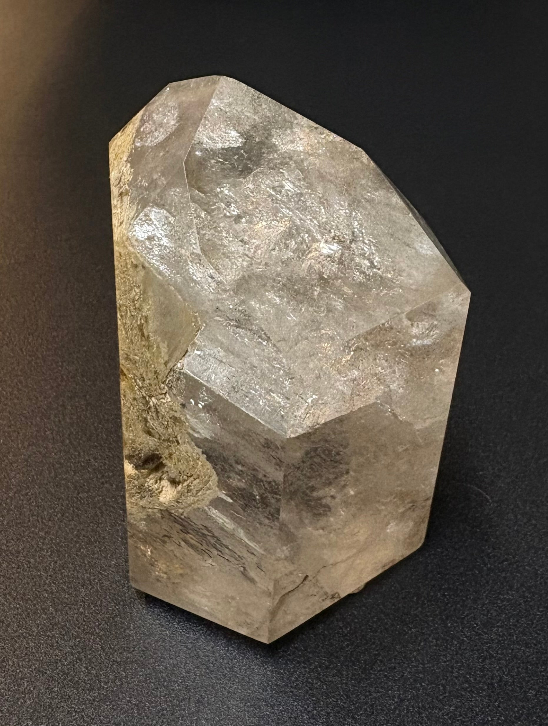 A raw, faceted quartz crystal cluster with natural inclusions, displayed on a dark textured background.