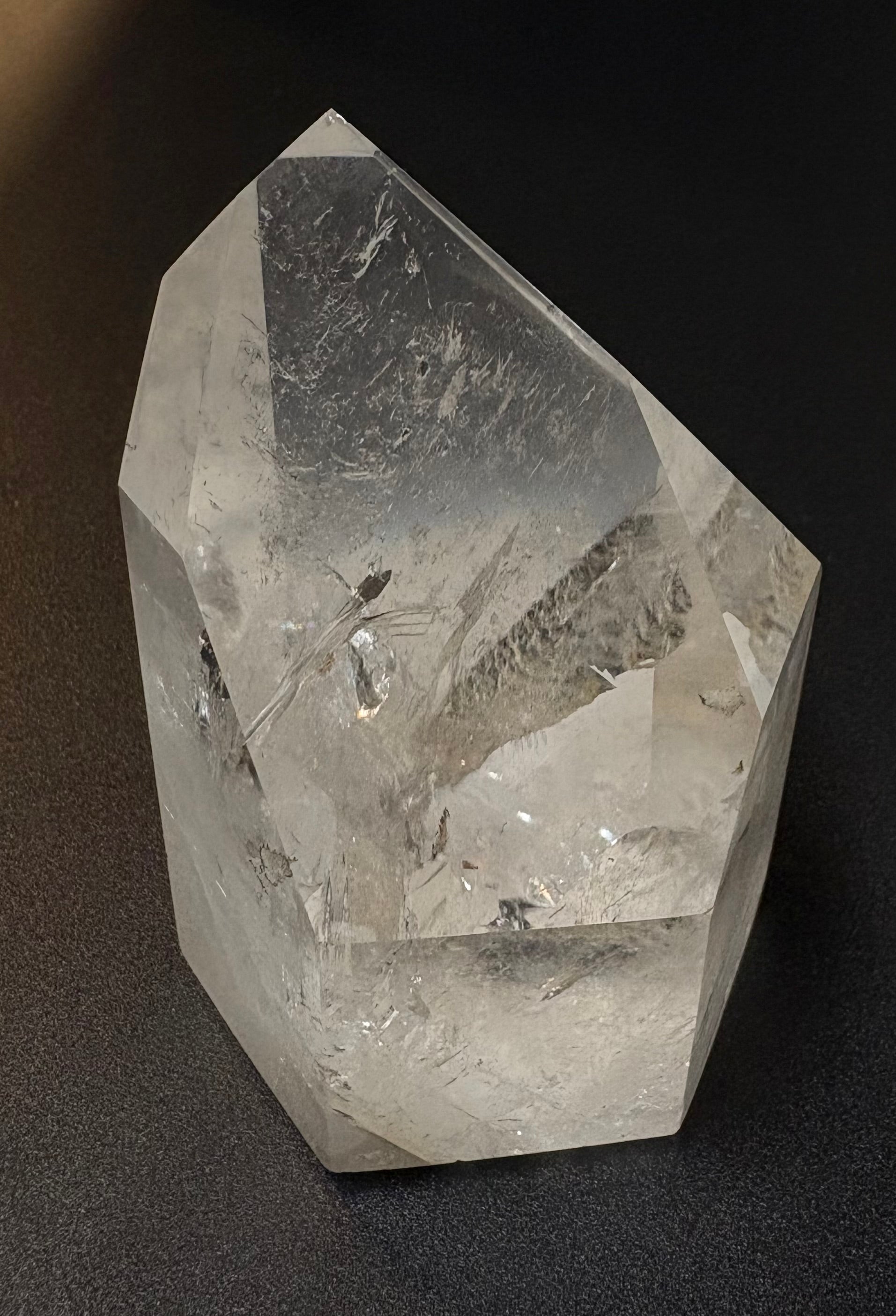 A clear quartz crystal point with natural inclusions, photographed on a dark textured background.