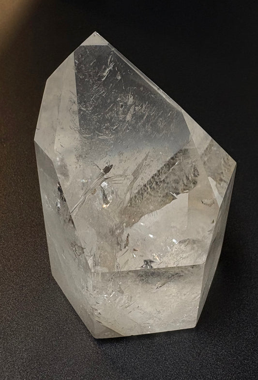 A clear quartz crystal point with natural inclusions, photographed on a dark textured background.