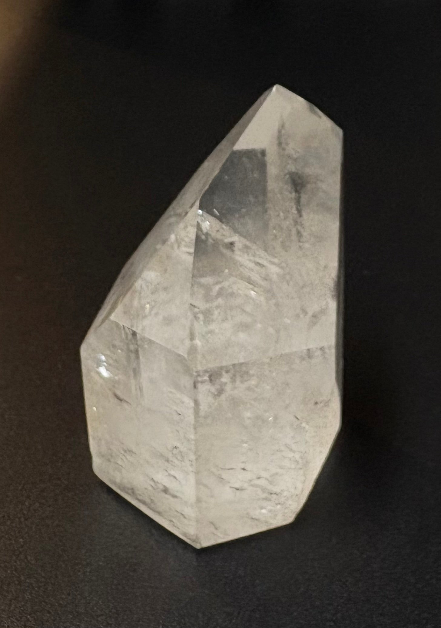 A clear faceted crystal tower or point-shaped stone photographed on a dark black background.