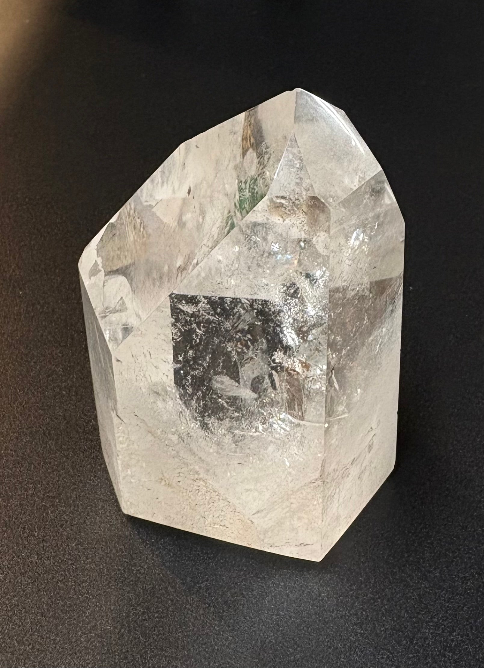 A raw, unpolished clear quartz crystal point with natural inclusions, photographed on a dark textured surface.