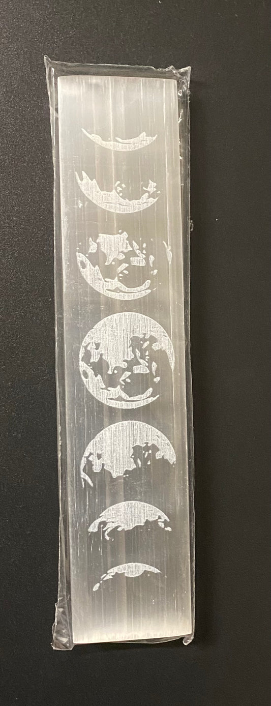 A selenite block featuring a vertical sequence of moon phases, sealed in a transparent plastic sleeve and photographed against a dark background.