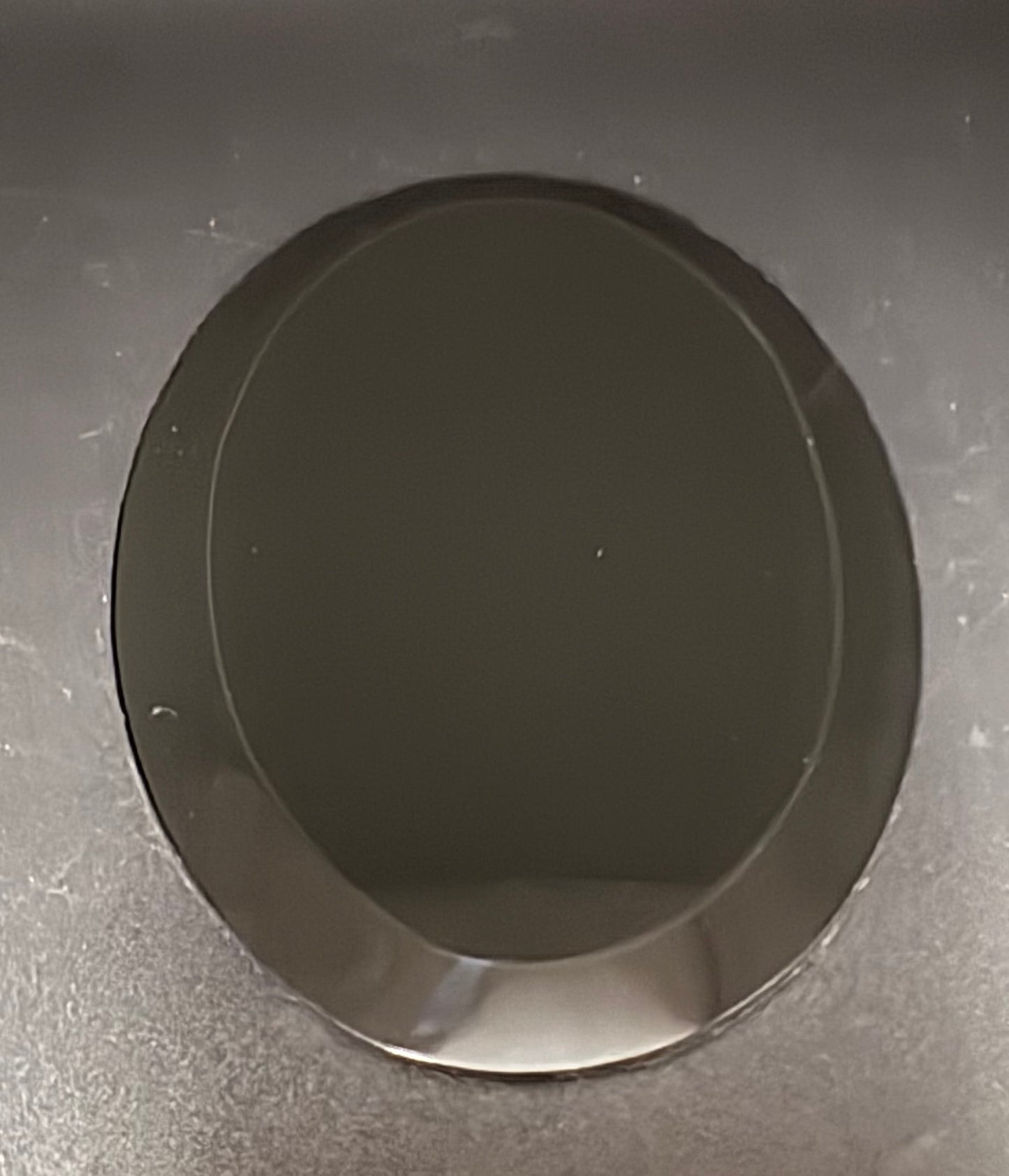 A dark gray oval-shaped mirror with a glossy, reflective surface, set against a textured dark gray background.