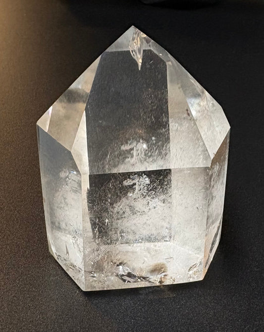 A clear faceted crystal tower or point with a hexagonal base, photographed on a dark black background.