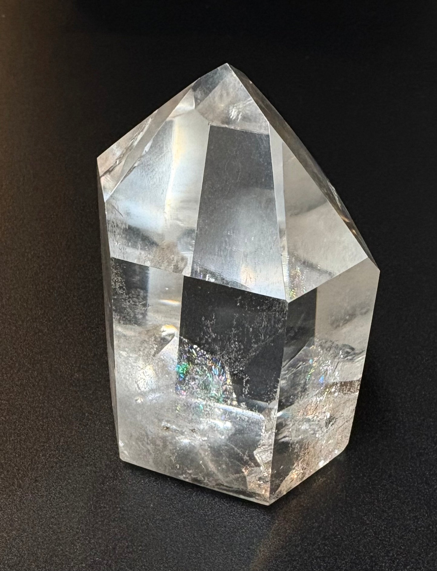 A clear quartz crystal point tower with natural inclusions, photographed on a dark textured background.