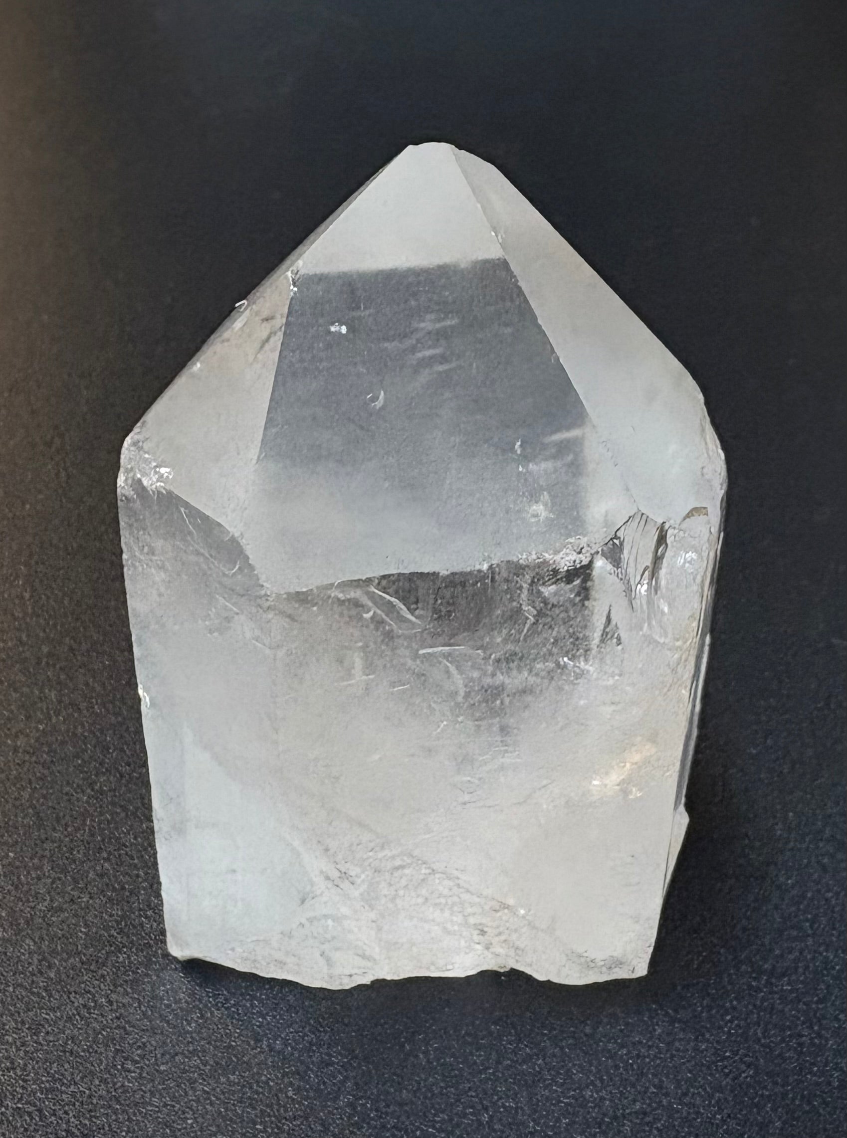 A clear quartz crystal point with natural rough edges, photographed on a dark textured background.