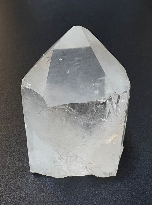 A clear quartz crystal point with natural rough edges, photographed on a dark textured background.