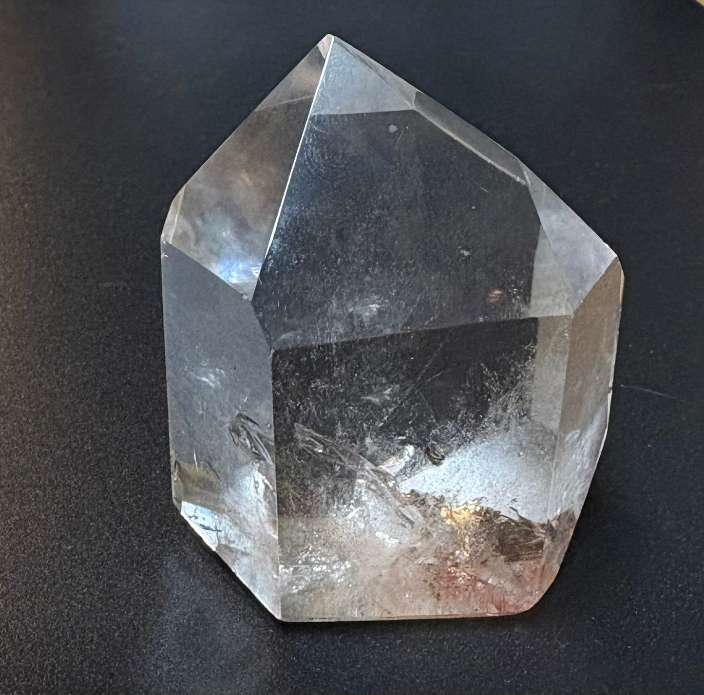 A natural clear quartz crystal point with internal inclusions, photographed on a dark textured surface.