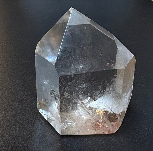 A natural clear quartz crystal point with internal inclusions, photographed on a dark textured surface.