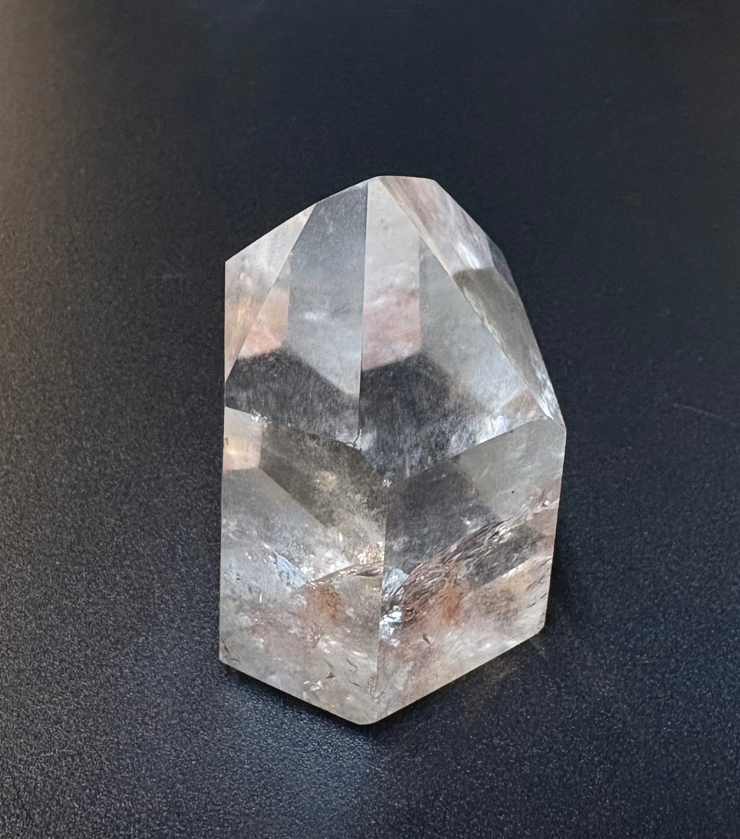 A natural clear quartz crystal point with faceted geometric edges, resting on a dark textured surface.