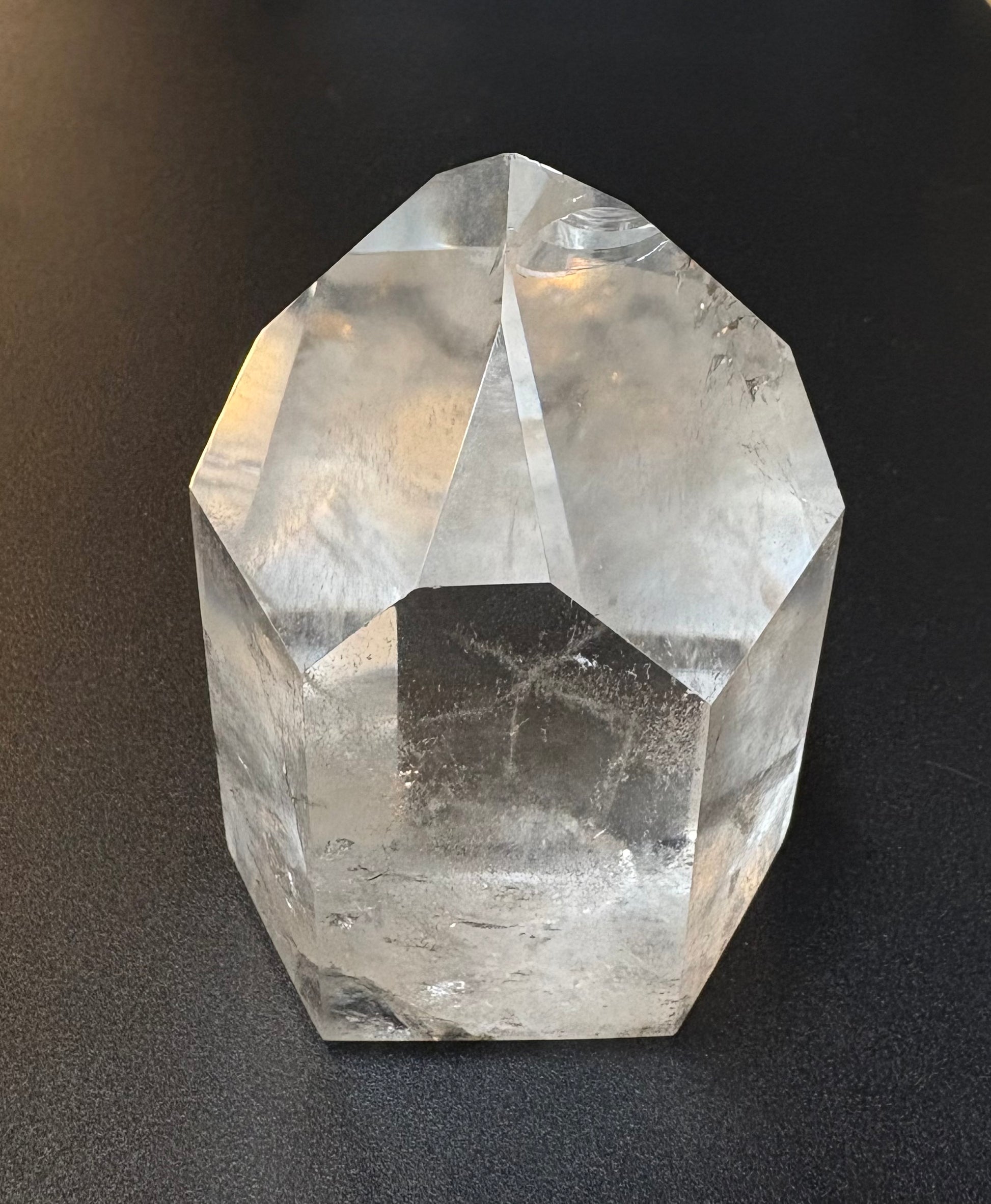 A faceted clear quartz crystal tower with a pointed top, resting on a dark textured surface.