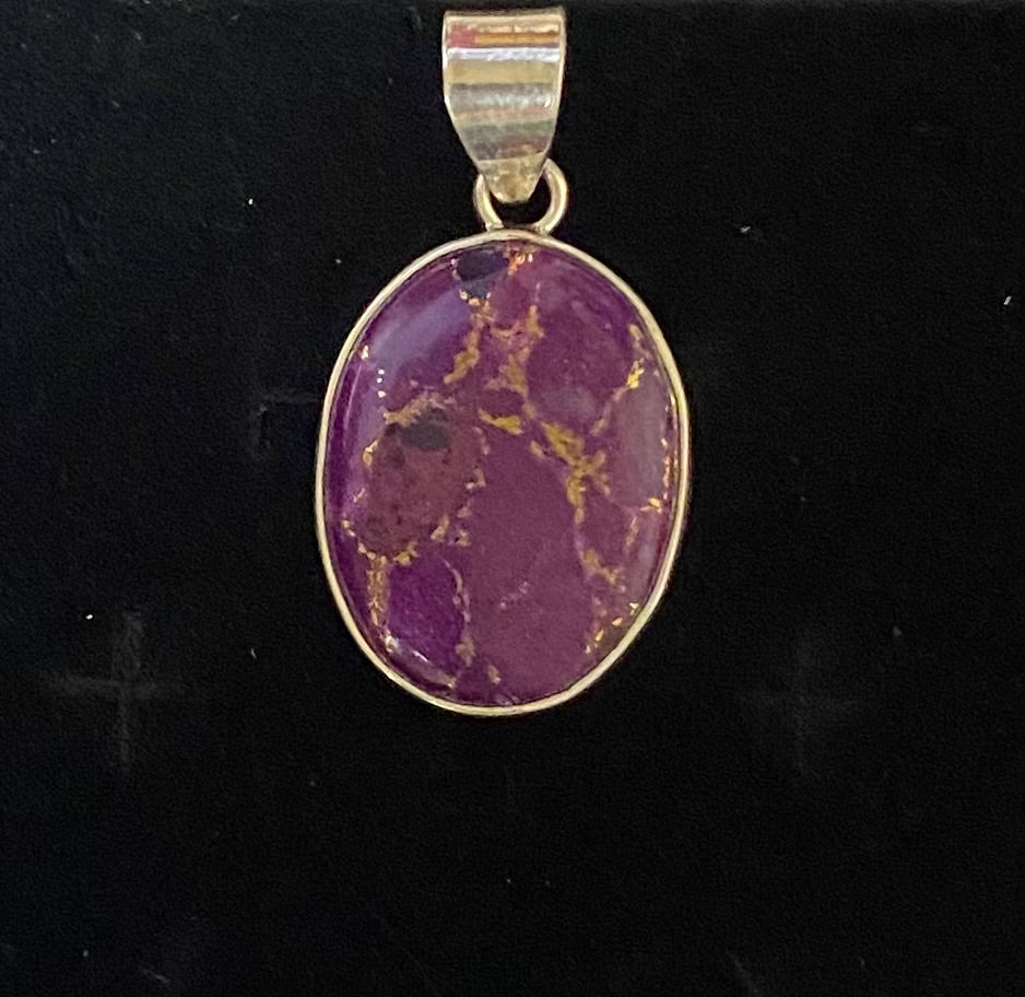 An oval pendant featuring a purple stone with prominent gold veining, set in a sterling silver bezel with a matching bail, displayed on a black background.