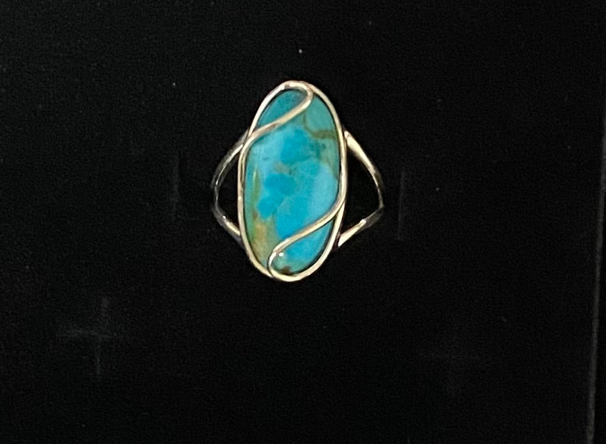 A silver ring featuring an oval turquoise stone with natural brown and cream matrix patterns, set in a wrap-style silver band against a black background.