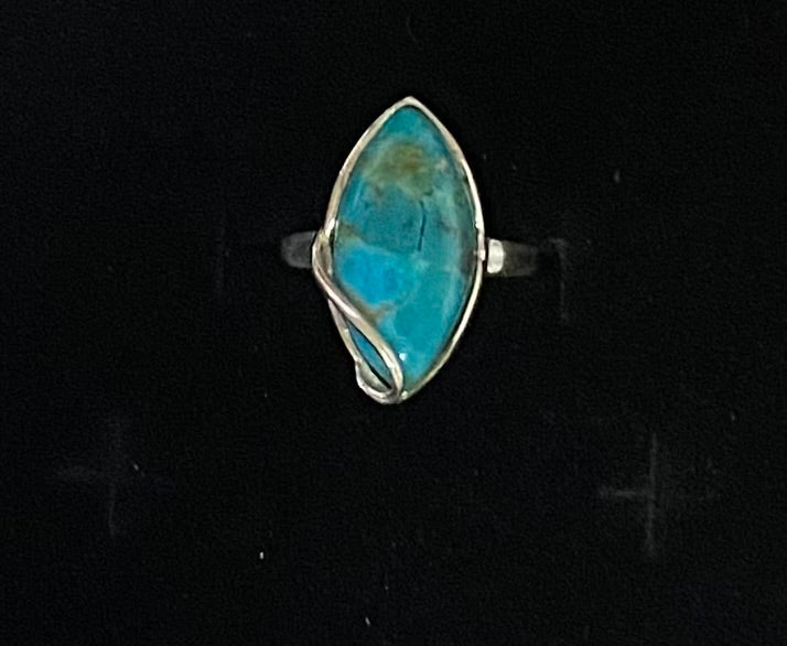 A silver ring featuring a marquise-shaped turquoise stone with natural brown matrix, set in a twisted wrap-style silver band against a black background.