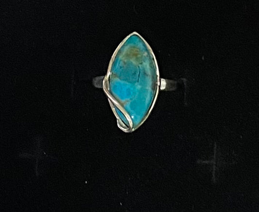 A silver ring featuring a marquise-shaped turquoise stone with natural brown matrix, set in a twisted wrap-style silver band against a black background.